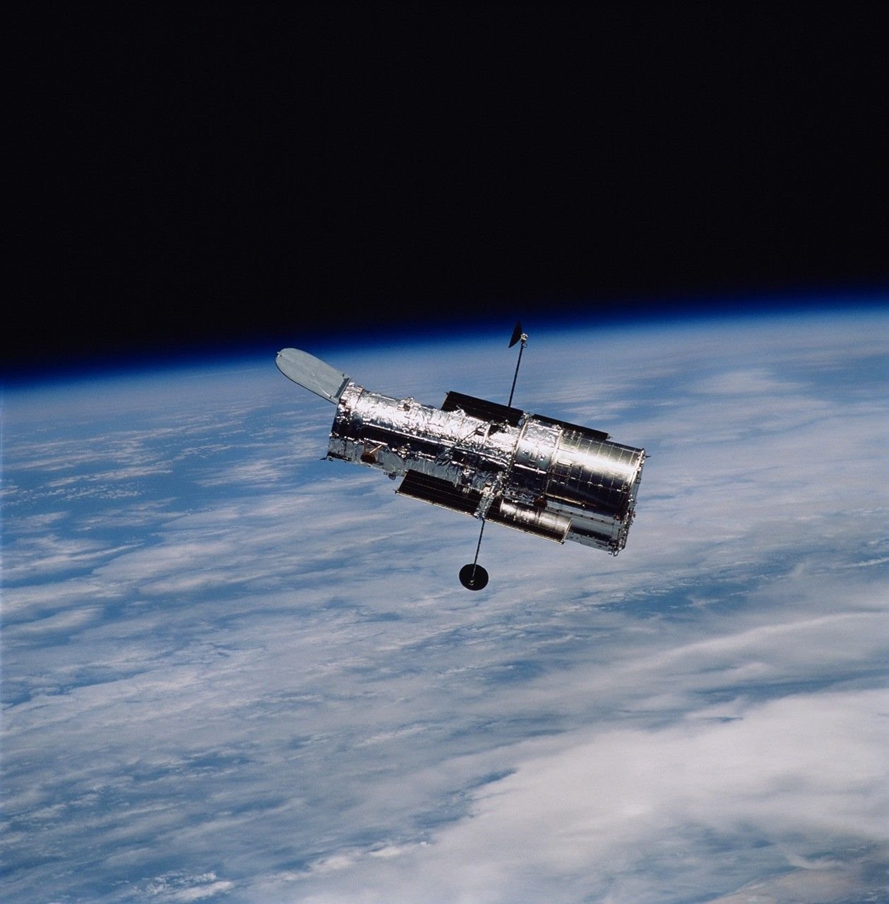 The silver Hubble Space Telescope floating in orbit above the blue and white curve of Earth