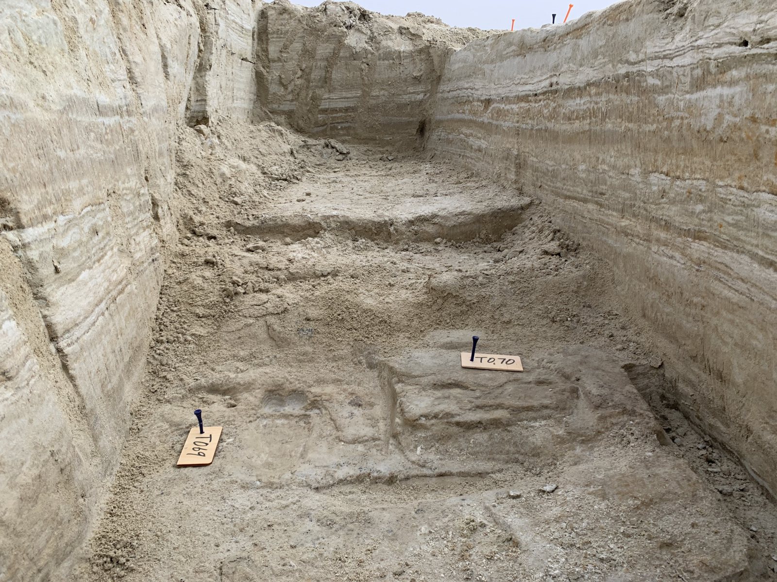 Numbered tags mark fossil human footprints at the bottom of a dug-out trench in white gypsum sediment